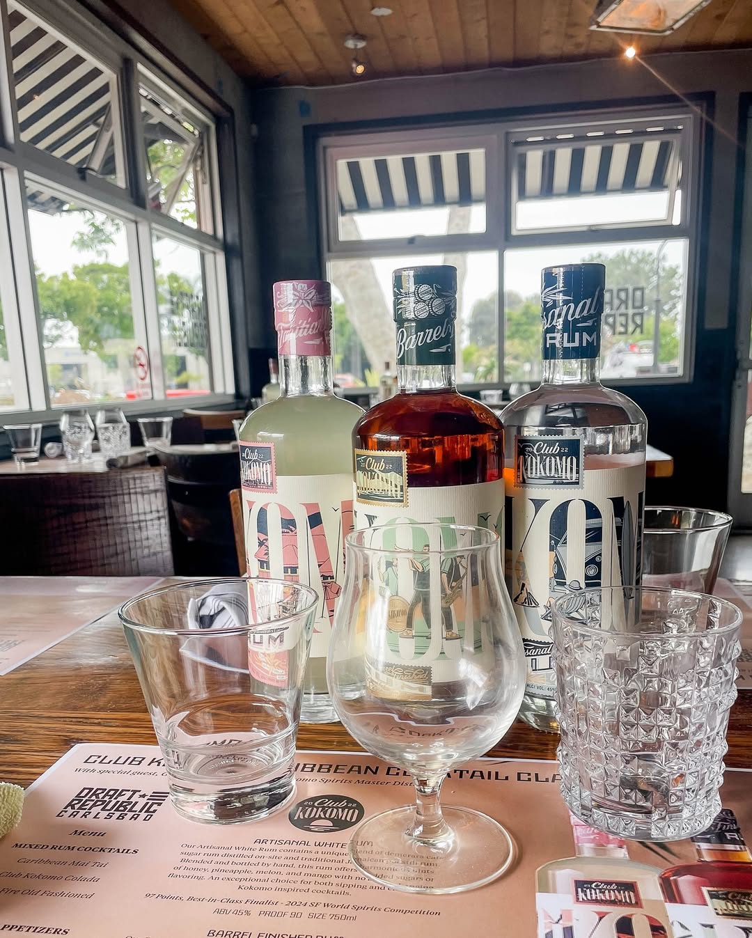 A close-up of three rum bottles arranged on a wooden table, set for a cocktails class with glassware and cocktail recipes.