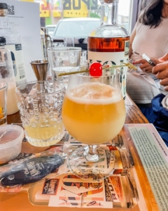 cocktails class mixed drink.jpg A freshly mixed tropical cocktail with a cherry garnish, surrounded by bar tools and ingredients at a cocktails class.