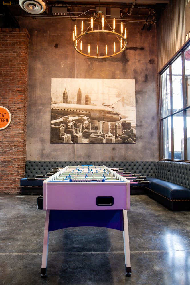 Foosball table in a stylish lounge at Draft Republic San Marcos, featuring industrial decor and leather seating.